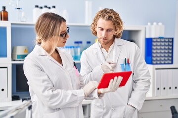 Man and woman wearing scientist uniform using touchpad at laboratory