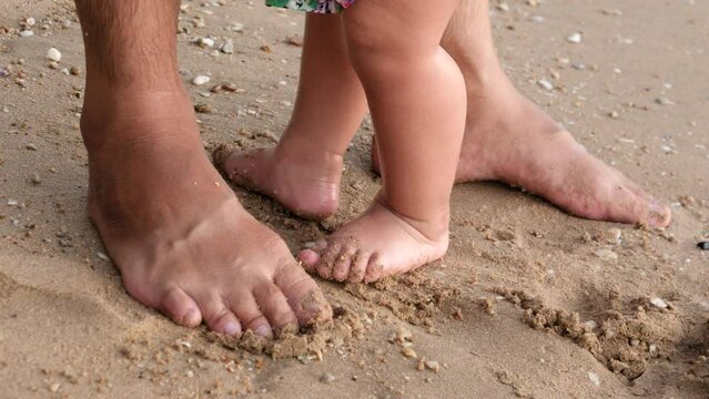 footage of feet child and father on sea beach, close-up