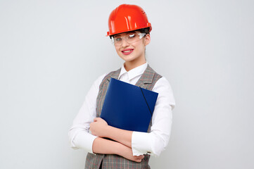 Young female caucasian engineer wearing orange constraction helmet and googles holds blueprint on...