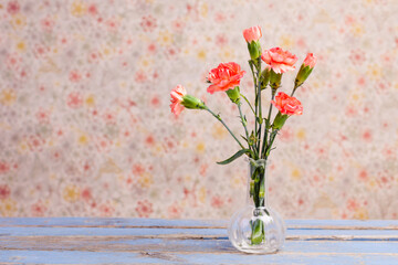 orange carnations in a glass vase infront of pattern wallpaper
