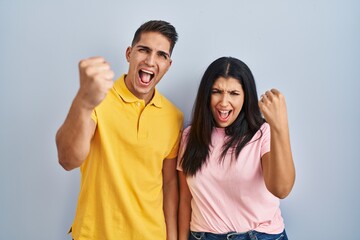 Fototapeta na wymiar Young couple standing over isolated background angry and mad raising fist frustrated and furious while shouting with anger. rage and aggressive concept.