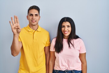 Fototapeta premium Young couple standing over isolated background showing and pointing up with fingers number four while smiling confident and happy.