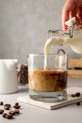 Pouring milk in glass with iced coffee. Cold refreshment summer sweet drink.