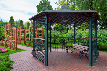 iron gazebo with a roof for relaxing on a wooden bench in the backyard with a vertical pergola for...