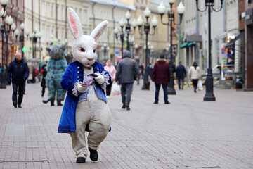 Person in Rabbit costume walking on a street. Bunny on crowd of people background, promoter in city