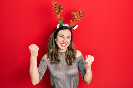 Young hispanic girl wearing deer christmas hat screaming proud, celebrating victory and success very excited with raised arms
