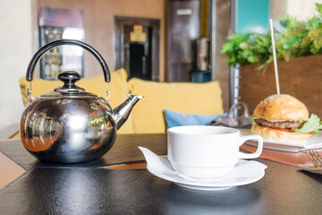 a white mug with tea and a metal teapot stand on a table in a cafe.selective focus