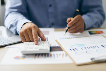 Businessman using a calculator to calculate numbers on a company's financial documents, analyzing...