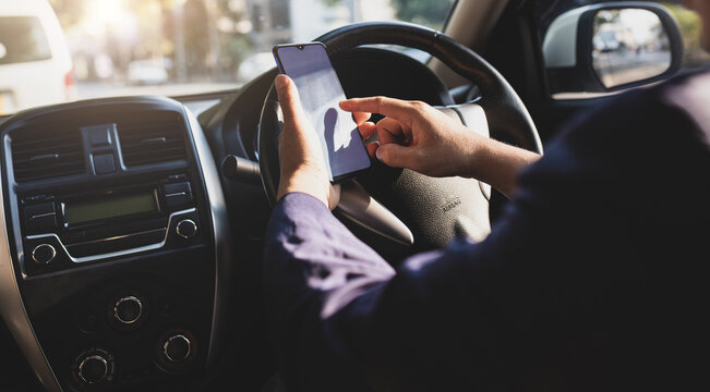 Businessman in car typing text on mobile phone to send text message while driving. Man using mobile phone looking at map while driving. Road safety and carelessness concepts.