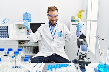 Fototapeta premium Middle age man working at scientist laboratory screaming proud, celebrating victory and success very excited with raised arms
