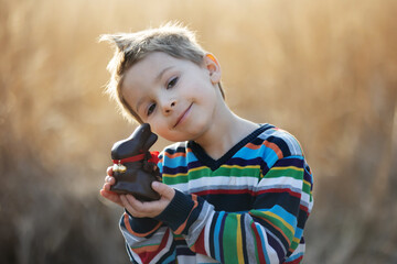 Beautiful stylish toddler child, boy, playing with Easter chocolate bunny in the park