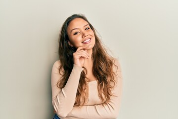 Young hispanic girl wearing casual clothes smiling looking confident at the camera with crossed arms and hand on chin. thinking positive.