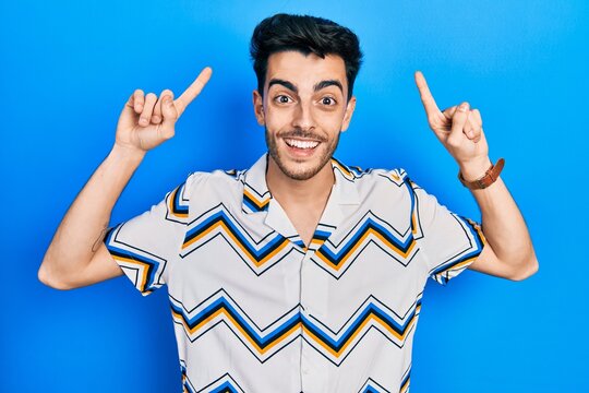 Young hispanic man wearing casual clothes smiling amazed and surprised and pointing up with fingers and raised arms.