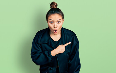 Young hispanic girl wearing sportswear surprised pointing with finger to the side, open mouth amazed expression.