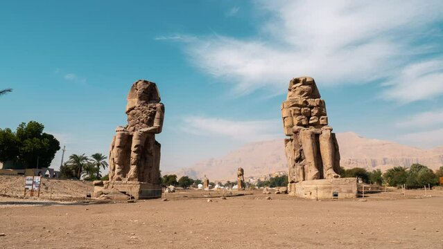 Colossi of Memnon on blue sky. Timelapse. Massive stone statues of Pharaoh Amenhotep III near Mortuary Temple. View from bottom between ancient monuments. Egyptian cultural heritage