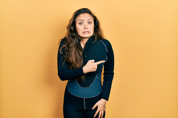 Young hispanic girl wearing diver neoprene uniform pointing aside worried and nervous with...