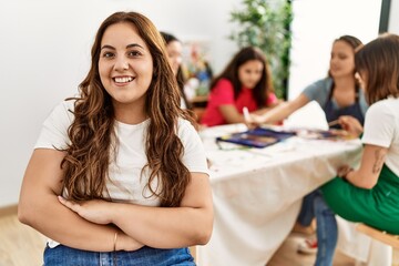 Group of women drawing sitting on the table. Hispanic woman smiling happy with arms crossed gesture at art studio.