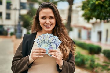Young hispanic woman smiling happy holding romania leu banknotes at the city.