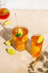 Iced tea with lemon, fresh mint leaves and ice in tall glasses with sun light and shadows.