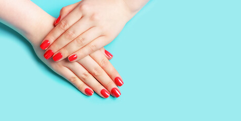 Female hands with red manicure on blue background, copy space.