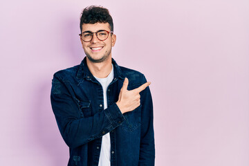 Young hispanic man wearing casual clothes and glasses cheerful with a smile of face pointing with hand and finger up to the side with happy and natural expression on face