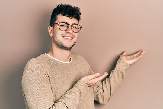 Young hispanic man wearing casual clothes and glasses inviting to enter smiling natural with open hand
