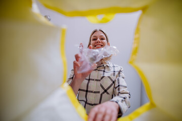 Image from inside yellow recycling bag of woman throwing a plastic bottle to recycle.