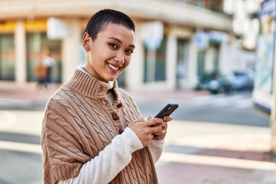 Young hispanic woman with short hair smiling happy using smartphone