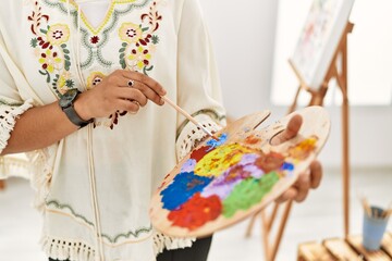 Young hispanic woman mixing color on palette at art studio
