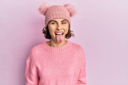 Young brunette woman wearing cute wool cap sticking tongue out happy with funny expression. emotion concept.