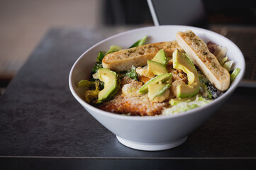 Focus on mixed salad with lettuce, chicken, avocado, parmesan cheese and toasted bread in a white big bowl. Healthy food and diet concept with copy space.