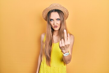 Young blonde girl wearing summer hat showing middle finger, impolite and rude fuck off expression