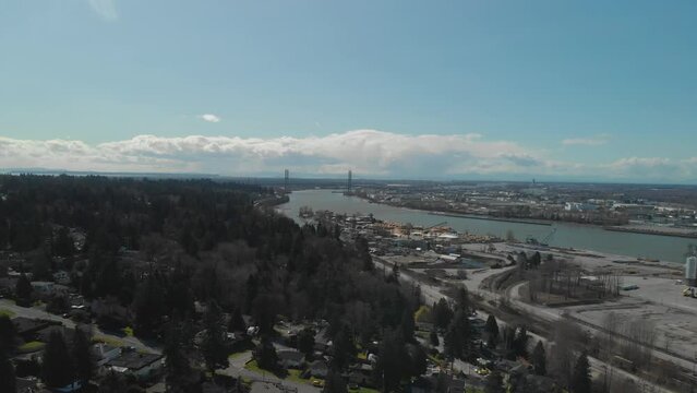 Scenic view of Delta BC on the edge of the Fraser river with the Alex Fraser bridge in the background Bright day blue sky clouds Aerial Wide reversing revealing homes neighbourhood below