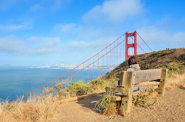 Lonely woman looking at scenery while sitting on a wooden bench facing San Francisco bay and the...