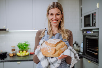 Happy woman holding homemade sourdough bread, cooking at home concept.