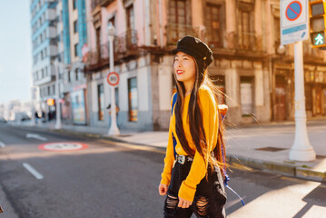 Young Asian girl with long hair walking around the city sightseeing. Happy Chinese woman crossing at a crosswalk.