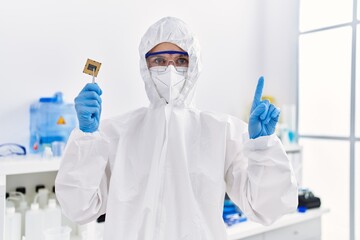 Young blonde woman holding cpu computer processor at laboratory surprised with an idea or question pointing finger with happy face, number one