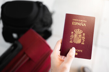 Close-up unrecognizable female hand holds Spanish European passport with unfocused luggage on background. Sunlight and flares. Travel concept.