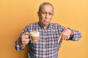 Handsome senior man with grey hair drinking a cup coffee pointing down looking sad and upset,...