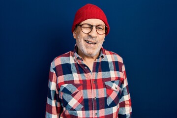 Handsome mature man wearing hipster look with wool cap winking looking at the camera with sexy...