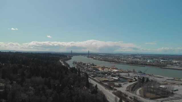 trucks cars traffic travelling along South perimeter high Delta BC Aerial wide high above trucking left and slowly panning right orbiting moving vehicles below Day blue sky clouds bridge in background