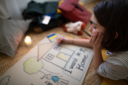 Sad Ukrainian refugee child missing her home and drawing her family. Ukrainian war concept.