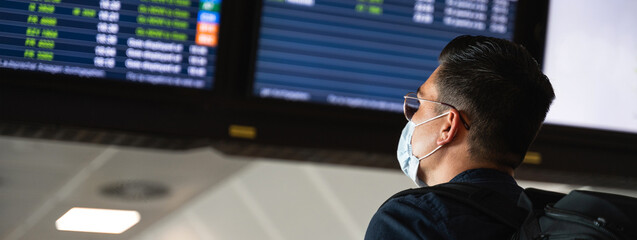 Horizontal banner or header Side view young man with face mask reading and checking the departures board in international airport