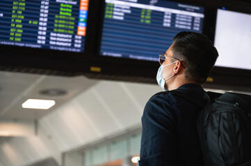 Fototapeta premium Side view young man with face mask reading and checking the departures board in international airport