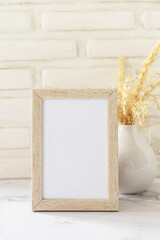 White picture frame mockup. White wall background. Scandinavian interior, neutral color palette with dry grass. Selective focus.