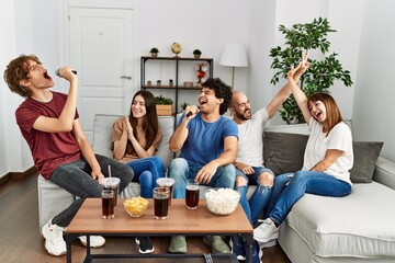 Group of young friends having party singing song using microphone at home.