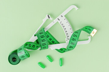 Weight loss concept. Measuring tape, pills and caliper on green background. Top view.
