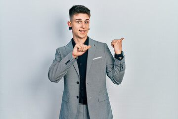 Young caucasian boy with ears dilation wearing business jacket pointing to the back behind with hand and thumbs up, smiling confident