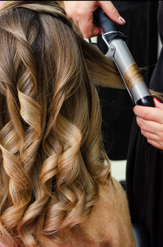 Stylist making a hairdo with hair curler. Beauty salon concept. Vertical