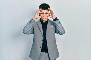 Young caucasian boy with ears dilation wearing business jacket trying to open eyes with fingers,...